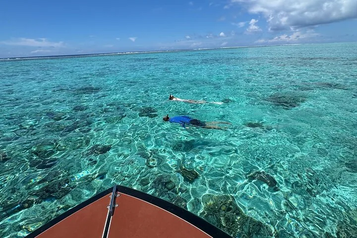 Two snorkelers floating over coral patches, seen from the boat's bow