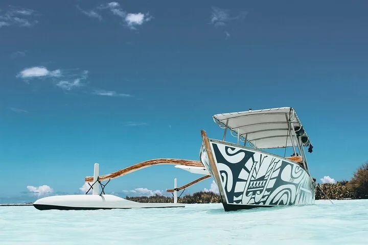Outrigger boat with a painted Polynesian pattern resting in white-sand shallows