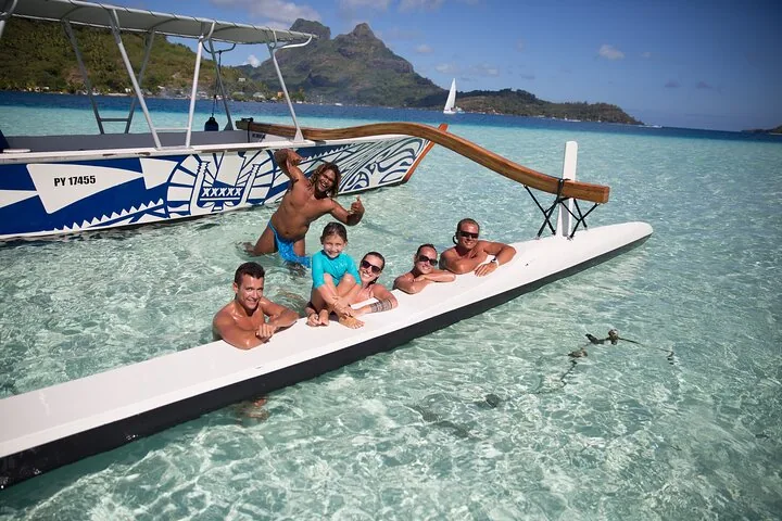 Guide and guests leaning on an outrigger beam in shallow water near small sharks