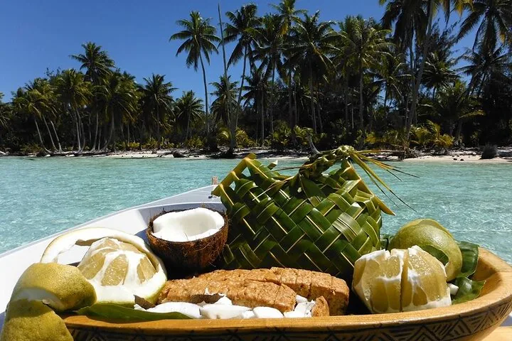 Coconut, fruit and a woven palm basket laid out by the water with palms behind