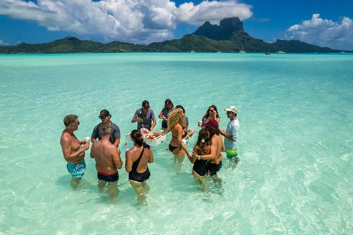 Guests standing waist-deep around a floating bar with Mount Otemanu behind