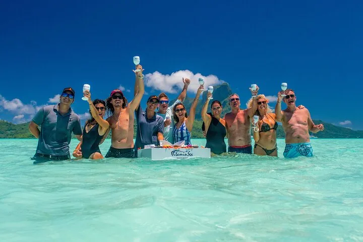 Group raising glasses in shallow water beside the floating bar box