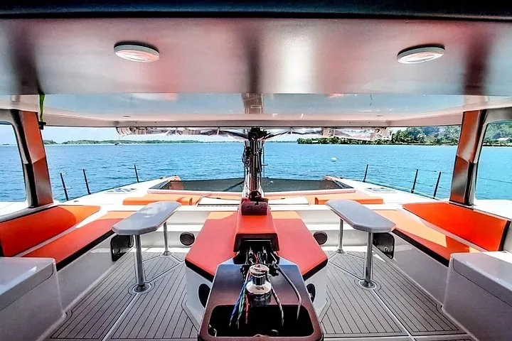 Shaded catamaran cockpit lounge with orange cushions and a steering wheel