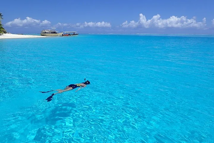 Snorkeler floating in bright blue water with boats moored offshore