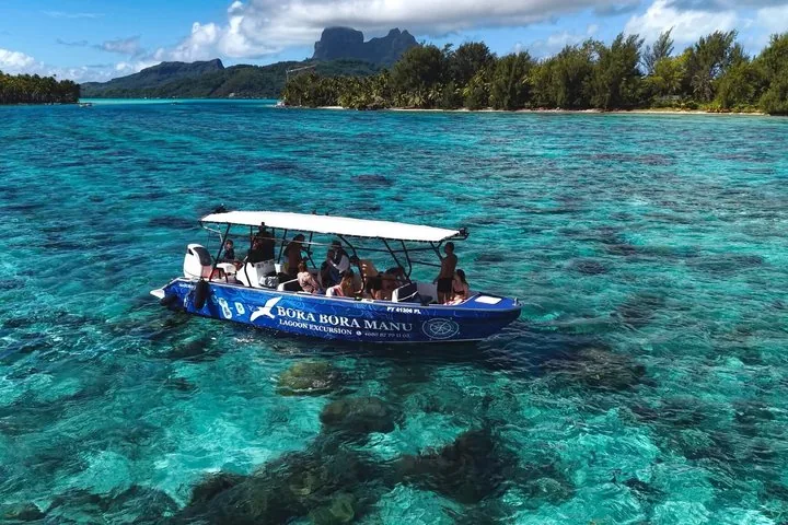 Covered boat full of guests anchored over coral in turquoise water