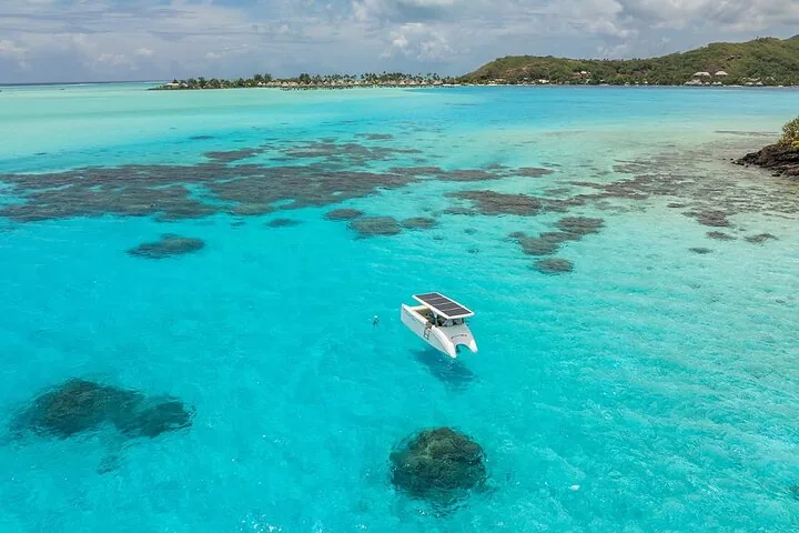 Solar boat above dark coral patches in a shallow lagoon, from above